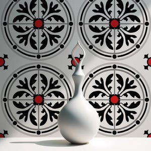 Może przedstawiać: Biały ceramiczny wazon o smukłej szyi i pękatej podstawie stoi na białej powierzchni. Tło przedstawia powtarzający się wzór czarnych i szarych okrągłych wzorów z czerwonymi akcentami.