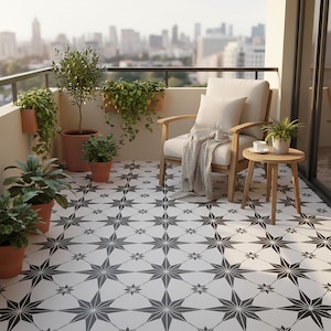 以下が含まれることがあります： 木製の椅子、クリーム色のクッション、小さなサイドテーブルがあるバルコニーのシーン。床は白黒の星柄です。鉢植えの植物と毛布があります。背景には都市の風景が見えます。