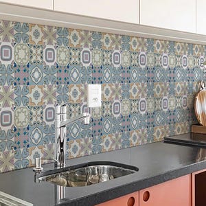 Puede incluir: Un salpicadero de cocina con baldosas estampadas en azul, gris y lavanda. Las baldosas tienen un diseño geométrico con elementos florales y de estrella. La encimera negra contrasta con los armarios de color rojo anaranjado. Se ven el fregadero y el grifo.