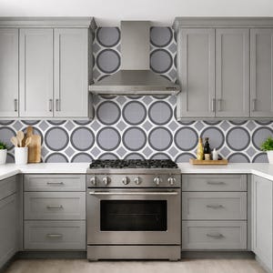 May include: A modern kitchen with gray cabinets, a stainless steel range, and a patterned backsplash. The kitchen features a U-shaped layout with white countertops and a stainless steel range hood. Decorative items include plants and wooden utensils.