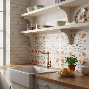 Op de afbeelding: Keukeninterieur met een witte spoelbak, messing kraan en houten werkbladen. Witte planken tonen kommen, borden en potten. De achterwand heeft een bloemenpatroon in oranje, groen en wit. Een kleine plant in een pot en een kom met citroenen.