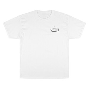 Puede incluir: Camiseta blanca con un pequeño gráfico en blanco y negro de un pastel con vapor saliendo. La camiseta tiene mangas cortas y cuello redondo. La camiseta está hecha de un material suave y cómodo.