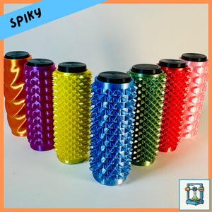 Op de afbeelding: Een verzameling kleurrijke cilinders met een getextureerd, stekelig oppervlak. De cilinders zijn in verschillende kleuren, waaronder oranje, paars, geel, blauw, groen, rood en roze. Elke cilinder heeft een zwarte bovenkant. Het woord "SPIKY" is zichtbaar linksboven.