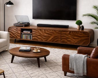 Könnte beinhalten: Ein modernes Wohnzimmer mit einem großen Flachbildfernseher über einem Holzmedienmöbel. Auf dem Möbel steht ein Plattenspieler. Ein helles Sofa, ein brauner Ledersessel und ein runder Couchtisch vervollständigen den Raum. Ein gemusterter Teppich und eine Topfpflanze sorgen für Wärme.