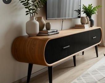 May include: A mid-century modern TV stand with a light wood top and black ribbed doors. The stand has rounded edges, black legs, and silver drawer pulls. Decorative vases and books sit on top.