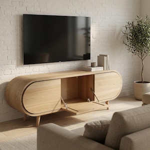 Peut inclure: Un meuble télé en bois clair aux extrémités arrondies, doté de deux placards latéraux et d'une porte centrale abattante. L'unité repose sur quatre pieds fuselés et présente une finition en grain de bois naturel pour le rangement.