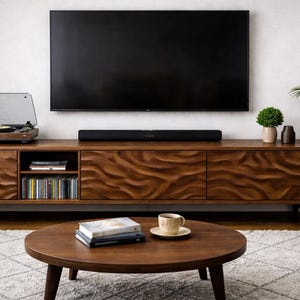 K&ouml;nnte beinhalten: Ein Wohnzimmer mit einem Holz-TV-Schrank mit wellenf&ouml;rmigem Design, einem gro&szlig;en Fernseher und einem runden Couchtisch. Der Schrank beherbergt einen Plattenspieler und CDs. Auf dem Tisch liegen B&uuml;cher und eine Kaffeetasse.
