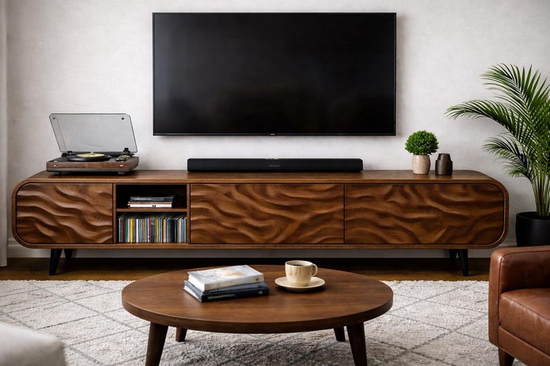 K&ouml;nnte beinhalten: Ein Wohnzimmer mit einem Holz-TV-Schrank mit wellenf&ouml;rmigem Design, einem gro&szlig;en Fernseher und einem runden Couchtisch. Der Schrank beherbergt einen Plattenspieler und CDs. Auf dem Tisch liegen B&uuml;cher und eine Kaffeetasse.