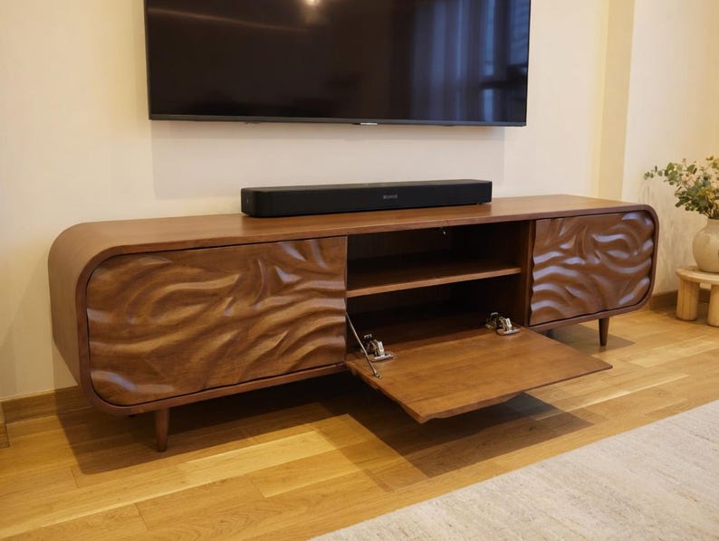 K&ouml;nnte beinhalten: Ein TV-Schrank aus Holz im Mid-Century-Modern-Stil mit geschwungenem Design und geschnitztem Wellenmuster auf den T&uuml;ren. Der Schrank hat ein offenes Regal und eine teilweise ge&ouml;ffnete T&uuml;r. Der Schrank ist braun, mit einer schwarzen Soundbar oben.