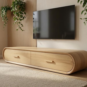 May include: A low-profile, light-colored wooden media console featuring a rounded, oval-shaped frame with two horizontal drawers. Each drawer is equipped with a simple, rectangular wooden handle, showcasing a smooth, natural wood grain finish.
