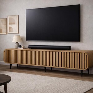 May include: A modern living room setup featuring a large black television mounted above a light wood cabinet with vertical slat detailing. A black soundbar sits on the cabinet. A potted plant and artwork complete the decor.