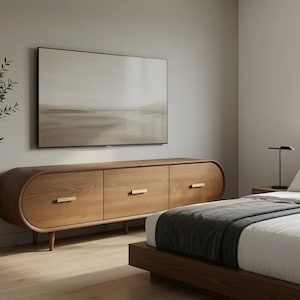 May include: A long, oval-shaped wooden media console featuring three cabinet doors with horizontal gold-toned metal handles. The console is mounted on short, tapered wooden legs and displays a natural wood grain finish in a warm brown tone.