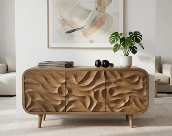 Puede incluir: Un aparador rectangular de madera con tres puertas de armario que presentan una textura tallada, ondulada y tridimensional. La pieza se apoya sobre cuatro patas cónicas y tiene un marco liso y redondeado. Discos de vinilo y auriculares negros descansan encima.