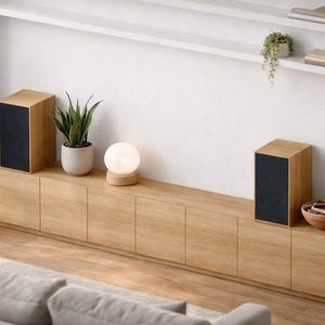 Puede incluir: Altavoces de madera con frentes de tela negra sobre un mueble largo de madera clara. Una peque&ntilde;a l&aacute;mpara redonda y plantas en macetas tambi&eacute;n est&aacute;n en el mueble. La habitaci&oacute;n tiene un dise&ntilde;o moderno y minimalista.
