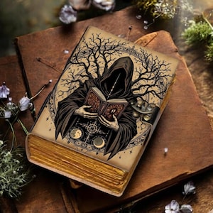 May include: A detailed illustration on a vintage book cover depicts a robed figure reading a book, with a tree and celestial elements. The book has gold-colored edges and is resting on a brown leather-bound book.