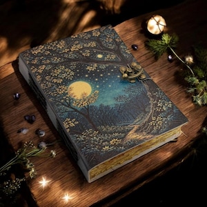 May include: A decorative journal with a forest and moon design. The cover depicts a night scene with a full moon, trees, and stars. The journal has a metal clasp and gold-coloured edges. The colour scheme is dark blue, gold, and brown.