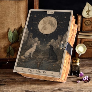 May include: A rectangular wooden box featuring a tarot card design titled The Moon on its front panel. The illustration depicts a large moon, two towers, a white wolf, a black wolf, and a lobster. A metal latch secures the side of the box.