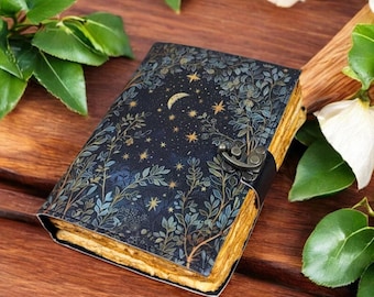 Puede incluir: Un diario azul oscuro con un diseño celestial con una luna creciente y estrellas. La cubierta está adornada con ilustraciones botánicas en tonos verdes y dorados. Tiene un cierre de metal y páginas envejecidas.