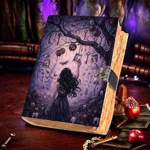 May include: A fantasy-themed journal with a detailed illustration. The cover depicts a woman reaching for a picture under a tree with hanging keys and red fruit. The journal has a metal clasp and aged, textured pages.