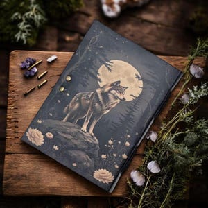 Può includere: Un diario di colore scuro con un'illustrazione di un lupo sotto la luna piena. La copertina raffigura un lupo su una roccia con uno sfondo di foresta. Il diario è aperto, rivelando le pagine interne. Il diario è su una superficie di legno.