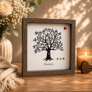 Peut inclure: Une œuvre d'art encadrée représentant un arbre noir avec des ornements bleus en forme d'œil comme feuilles. Un petit cœur rouge et trois oiseaux colorés sont également inclus. L'œuvre est personnalisée avec le nom "Hendricks" et a un cadre en bois rustique.