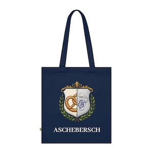 May include: Navy blue tote bag featuring a crest design with a pretzel and a beer stein. The crest is surrounded by a green wreath and the text "ASCHEBERSCH" is printed below the crest. The bag has navy blue handles.