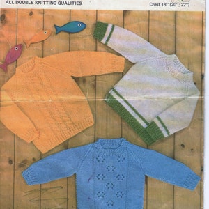 May include: Three knitted sweaters for children. The sweaters are orange, white with green stripes, and blue. The sweaters are laid out on a wooden surface. The image includes the text "Lee Target" and "8839 1/- 8p Chest 18" (20"; 22")".