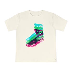 Puede incluir: Camiseta color crema con un gráfico colorido de un zapato en tonos azules, verdes, morados y rosas. El diseño tiene un efecto en capas y abstracto. La camiseta tiene mangas cortas y cuello redondo.