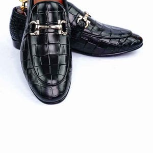 May include: Black leather loafers with a crocodile texture. The shoes have a silver-colored buckle and a rounded toe. The loafers are displayed on a white background. The shoes are a classic style.