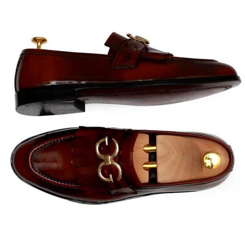 Puede incluir: Mocasines de cuero marr&oacute;n con hebillas doradas. Los zapatos tienen un acabado brillante y un dise&ntilde;o cl&aacute;sico. La imagen muestra los zapatos desde dos &aacute;ngulos, destacando su construcci&oacute;n y estilo. Un calzado elegante.