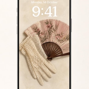 Può includere: Uno smartphone che mostra uno sfondo digitale con un paio di guanti in pizzo color crema e un ventaglio pieghevole rosa con motivo floreale. Lo schermo mostra l'ora 9:41 e la data lunedì 14 ottobre su uno sfondo color beige chiaro.