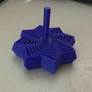 May include: A blue, star-shaped object with a central vertical post. The object has multiple layers, each a smaller star shape, creating a layered effect. The design is a solid, geometric form.