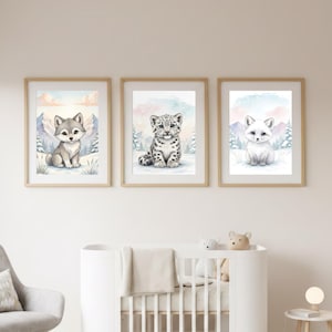 May include: Three framed watercolor prints featuring adorable winter animals. The prints include a wolf, a snow leopard, and a white arctic fox, all set against a snowy mountain backdrop. The frames are a light wood color.
