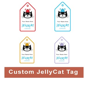 May include: Four custom JellyCat tags in red, blue, yellow, and purple, each featuring a black cat with a hat. The tags include the text "Your Name Here", "JELLYCAT LONDON". A brown banner below reads "Custom JellyCat Tag".