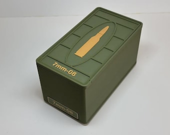 Può includere: Una scatola rettangolare verde oliva con un disegno in rilievo sul coperchio con una forma di proiettile color oro. Il testo "7mm-08" è stampato sul coperchio e sul lato della scatola.