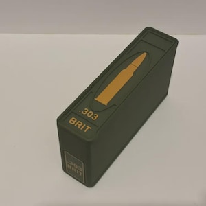 以下が含まれることがあります： 金色の弾丸のデザインと「.303 BRIT」の文字が入った、オリーブグリーンの長方形の箱。箱はわずかに傾斜した上部と、側面に同じテキストの小さなラベルが付いています。