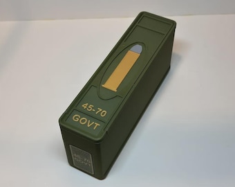 May include: An olive green rectangular box with a gold-colored bullet graphic and the text "45-70 GOVT". The box has a hinged lid and a small rectangular label on the side with the same text.