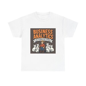 May include: White t-shirt with a graphic of a cowboy herding white cats. The text "BUSINESS ANALYTICS" is above the image, with "Like herding cats on Meth" below. The design uses brown, orange, and blue colours.