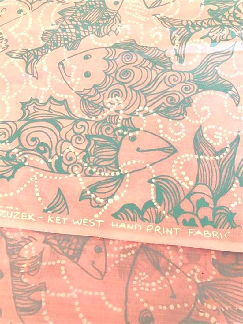 Peut inclure: Tissu rose avec un motif de poissons turquoise. Les poissons sont stylis&eacute;s avec des d&eacute;tails tourbillonnants et des lignes pointill&eacute;es blanches. Le texte "ZUZEK - KEY WEST HAND PRINT FABRIC" est imprim&eacute;.