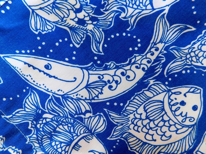 Peut inclure: Gros plan sur un tissu bleu et blanc avec un motif de poissons r&eacute;p&eacute;t&eacute;. Les poissons sont stylis&eacute;s avec des contours d&eacute;taill&eacute;s et des &eacute;l&eacute;ments d&eacute;coratifs. Le fond est bleu uni, et le design &eacute;voque un th&egrave;me nautique.