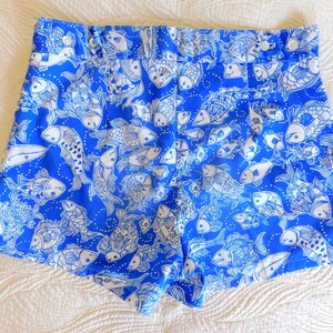 Peut inclure: Short bleu vif avec un motif de poissons blancs. Le short a une taille haute et une fermeture boutonn&eacute;e. Le tissu est d'un bleu vif avec un motif r&eacute;p&eacute;t&eacute; de divers dessins de poissons.