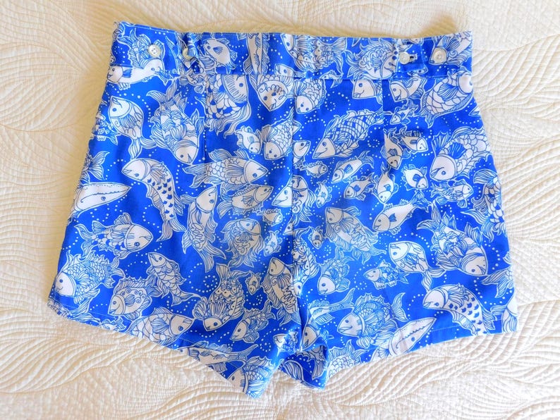 Peut inclure: Short bleu vif avec un motif de poissons blancs. Le short a une taille haute et une fermeture boutonn&eacute;e. Le tissu est d'un bleu vif avec un motif r&eacute;p&eacute;t&eacute; de divers dessins de poissons.