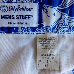 Peut inclure: Gros plan sur un tissu &agrave; motifs bleu et blanc avec une doublure blanche. Le tissu pr&eacute;sente un motif de poisson. Les &eacute;tiquettes indiquent "Lilly Pulitzer MENS STUFF PALM BEACH" et "65% POLYESTER 35% COTTON". La taille est de 76 cm.