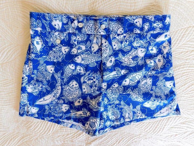 Peut inclure: Short bleu avec un motif de poissons blancs. Le short a une fermeture boutonn&eacute;e et est fait d'un tissu l&eacute;ger. Le motif de poissons comprend diverses esp&egrave;ces et tailles, cr&eacute;ant un look estival et ludique.