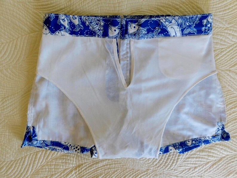 Peut inclure: Short de bain blanc avec un motif de poissons bleu et blanc sur les bords. Le short a une doublure blanche et une fermeture &eacute;clair &agrave; l'avant. Le tissu semble l&eacute;ger, adapt&eacute; &agrave; la natation. Mesures en centim&egrave;tres.