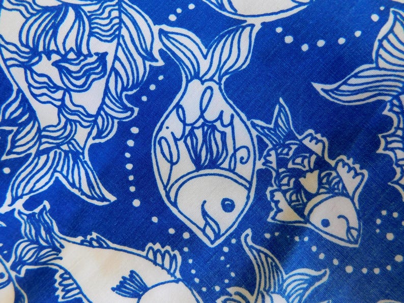 Peut inclure: Gros plan sur un tissu avec un motif de poissons bleu et blanc. Les poissons sont soulign&eacute;s en bleu sur un fond blanc, avec un design stylis&eacute;. Le mot "Lilly" est &eacute;crit &agrave; l'int&eacute;rieur d'un des poissons.