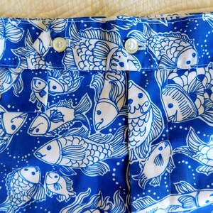 Peut inclure: Gros plan sur un tissu bleu avec un motif de poissons blancs. Le tissu pr&eacute;sente un motif r&eacute;p&eacute;t&eacute; de poissons stylis&eacute;s, avec des d&eacute;tails tels que des nageoires et des &eacute;cailles. Le tissu est fronc&eacute; et comporte des boutons visibles.