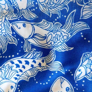 Peut inclure: Gros plan sur un tissu bleu et blanc avec un motif de poissons. Le motif pr&eacute;sente des poissons blancs stylis&eacute;s avec le mot "Lilly" &eacute;crit sur certains d'entre eux, sur un fond bleu vif. Les poissons sont soulign&eacute;s en blanc.