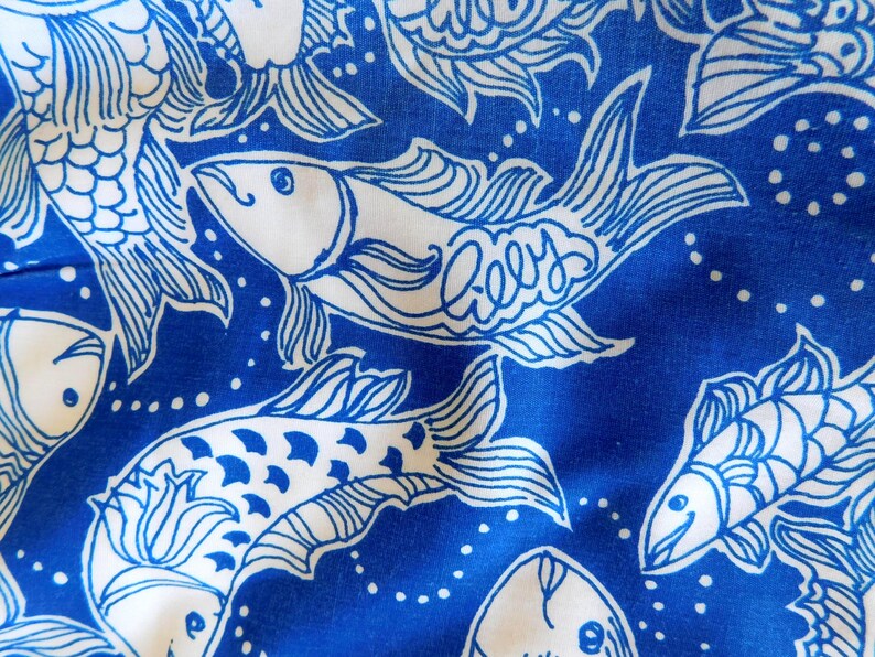 Peut inclure: Gros plan sur un tissu bleu et blanc avec un motif de poissons. Le motif pr&eacute;sente des poissons blancs stylis&eacute;s avec le mot "Lilly" &eacute;crit sur certains d'entre eux, sur un fond bleu vif. Les poissons sont soulign&eacute;s en blanc.