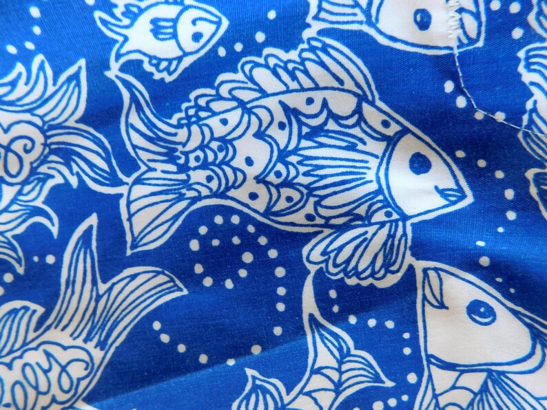 Peut inclure: Gros plan sur un tissu bleu avec un motif de poissons blancs. Les poissons sont stylis&eacute;s avec des nageoires et des &eacute;cailles d&eacute;taill&eacute;es, et le fond pr&eacute;sente de petits points blancs. Le motif se r&eacute;p&egrave;te sur le tissu.